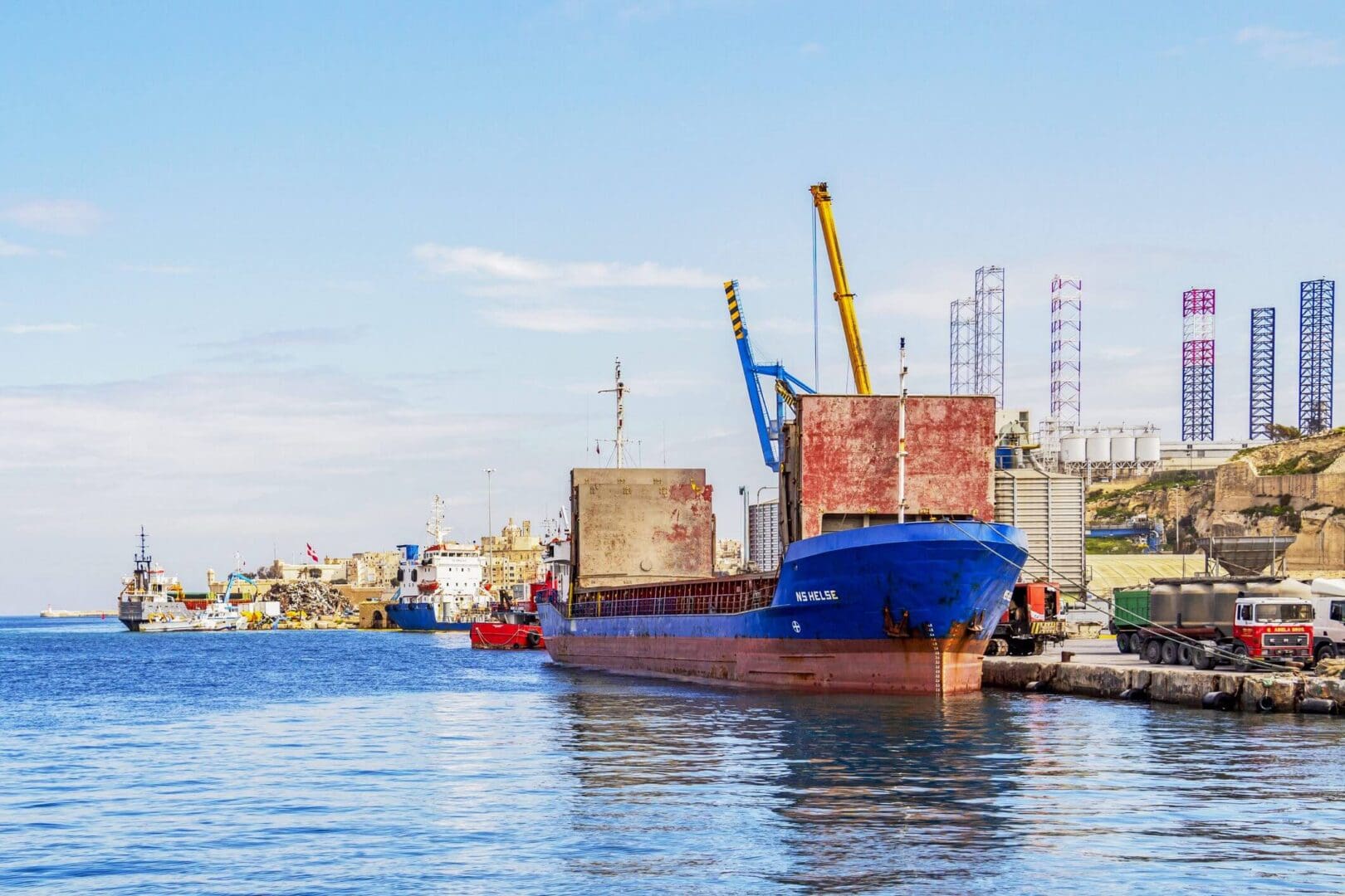 Cargo ship docked at a busy industrial port with cranes.